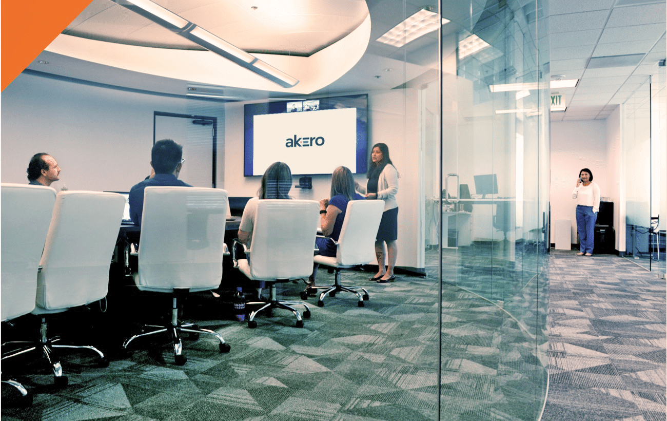 A group meets for a presentation in a glass-walled conference room, while a woman talks on the phone in the background