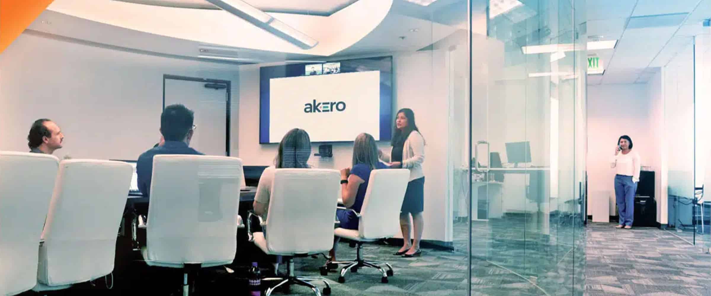 A group meets for a presentation in a glass-walled conference room, while a woman talks on the phone in the background