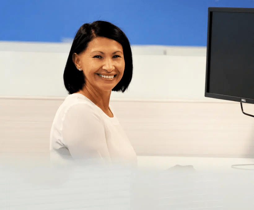 A female Akero employee sitting at a computer on a cubicle smiles at the camera
